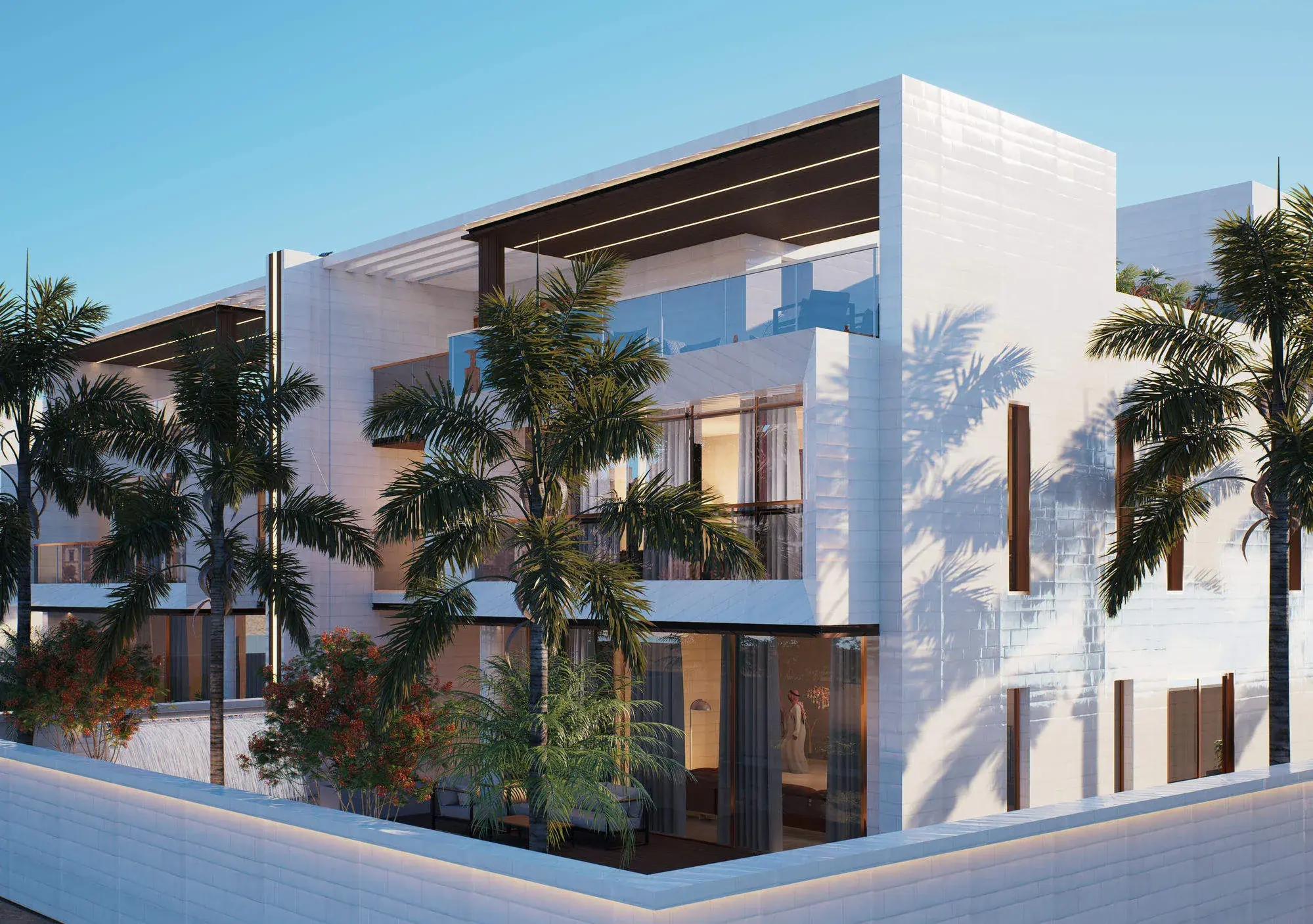 Corner of the twin villa by day: white stone-clad volumes under a timber pergola, glass balustrades to the roof terrace, royal palms and flowering trees against a low boundary wall.