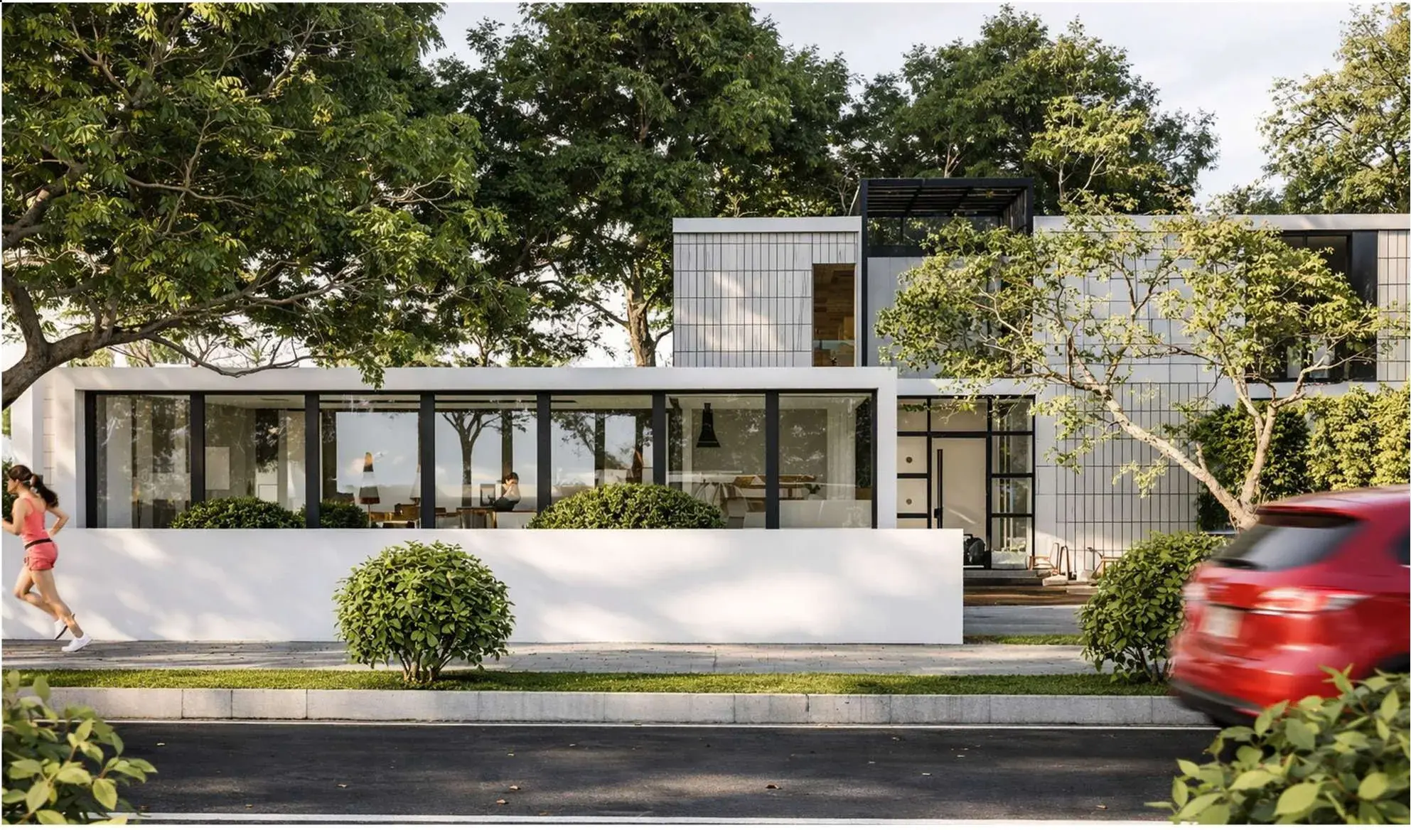 Street elevation: a low white boundary wall, full-height glazing to the ground floor and a gridded upper volume screened by mature trees.